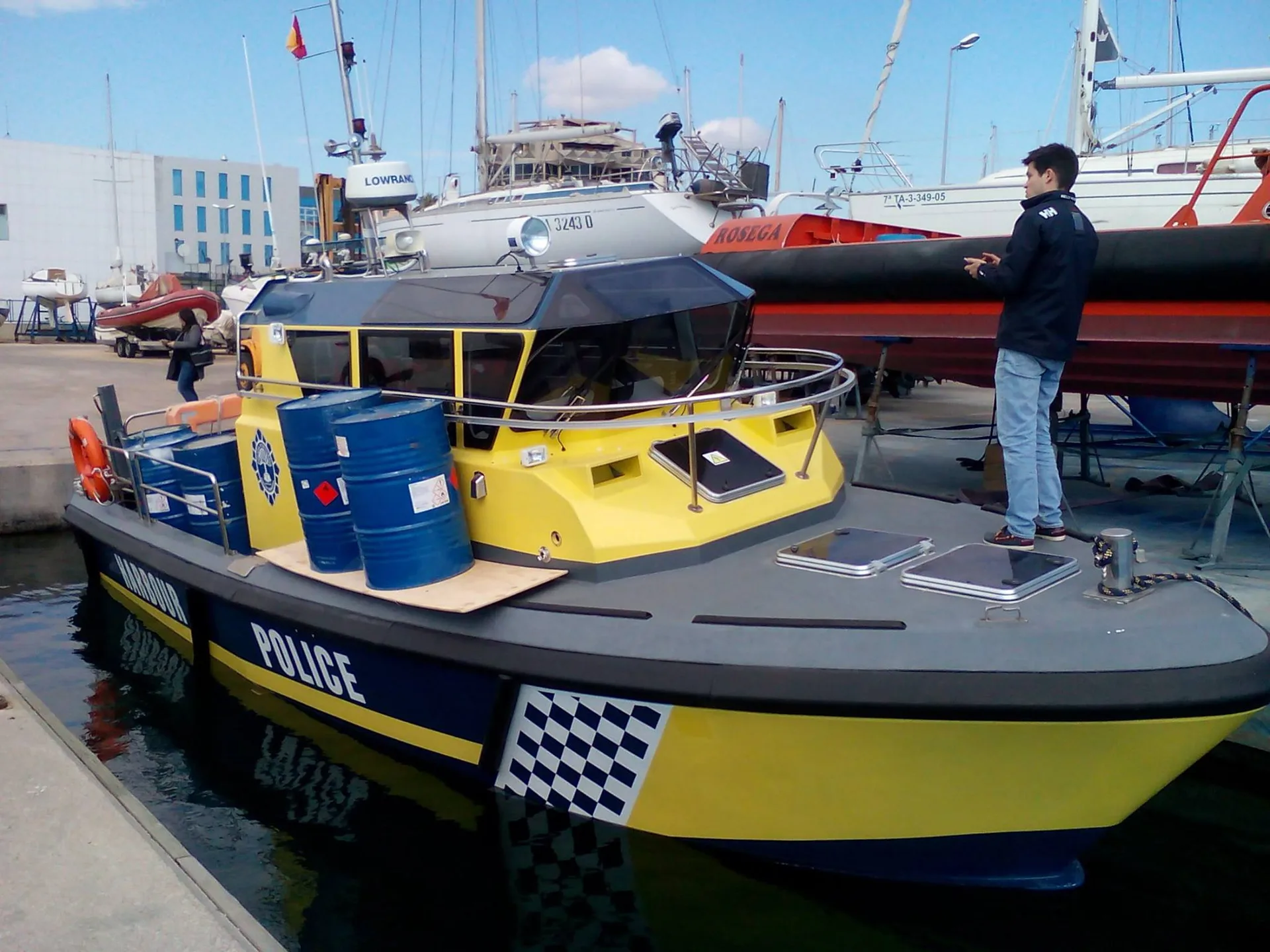 Embarcación de trabajo profesional amarilla operando en puerto, con tripulación a bordo.